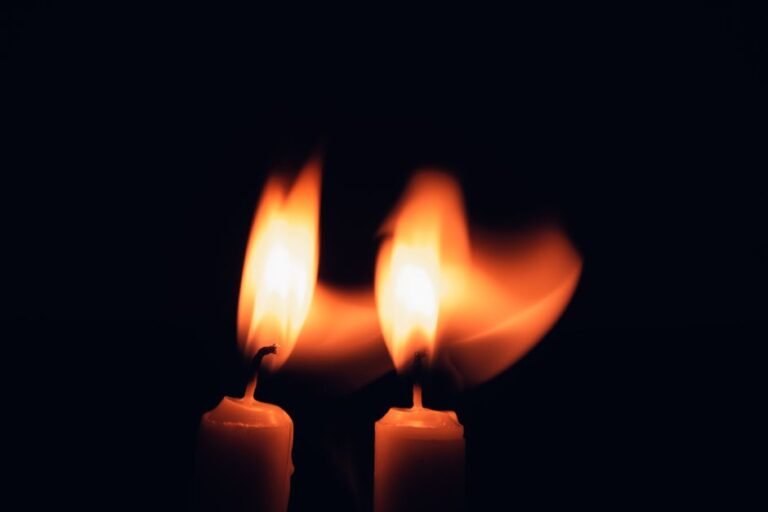 Deux bougies dont les flammes se penchent l’une vers l’autre dans l’obscurité