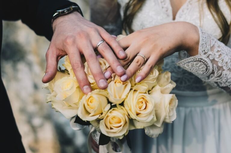 Mains des mariés et alliances au-dessus d’un bouquet de roses