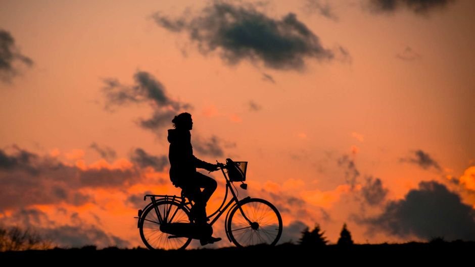 Silhouette d'une personne à vélo devant un ciel de coucher de soleil