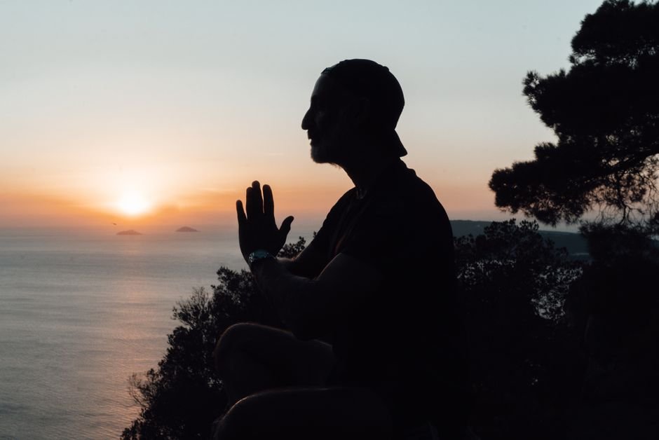 Silhouette d’un homme en méditation, mains jointes, au coucher du soleil