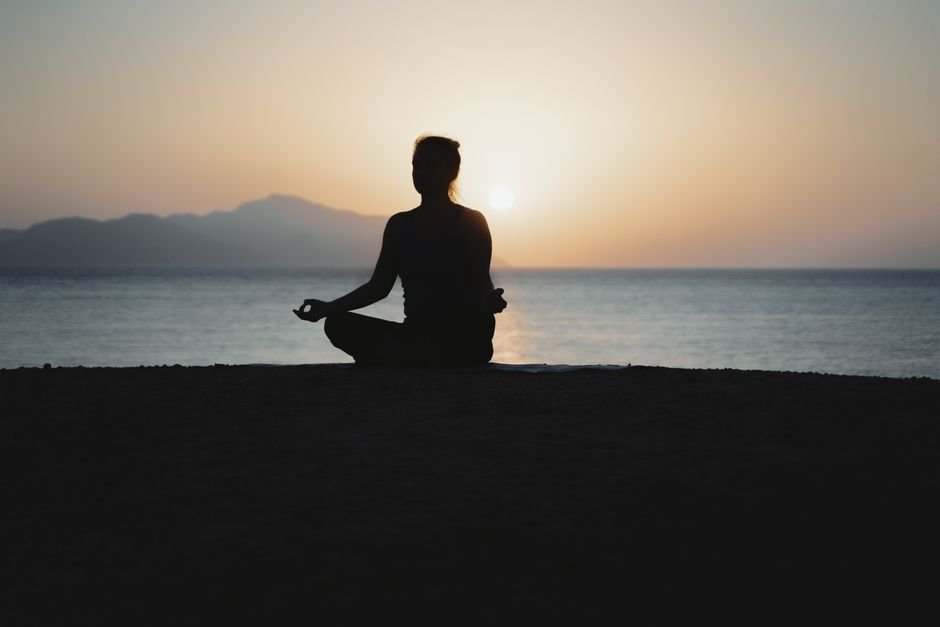Silhouette d’une femme en méditation face à la mer au coucher du soleil