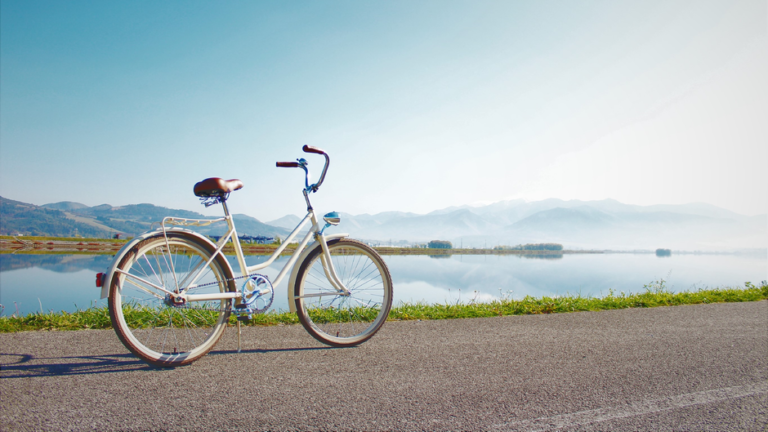 Vélo blanc posé au bord d'un lac calme avec des montagnes brumeuses